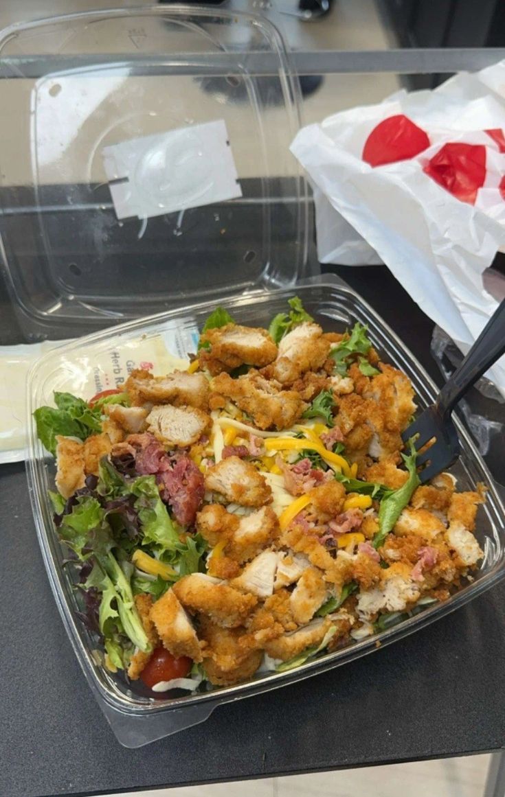 a plastic container filled with salad and meat