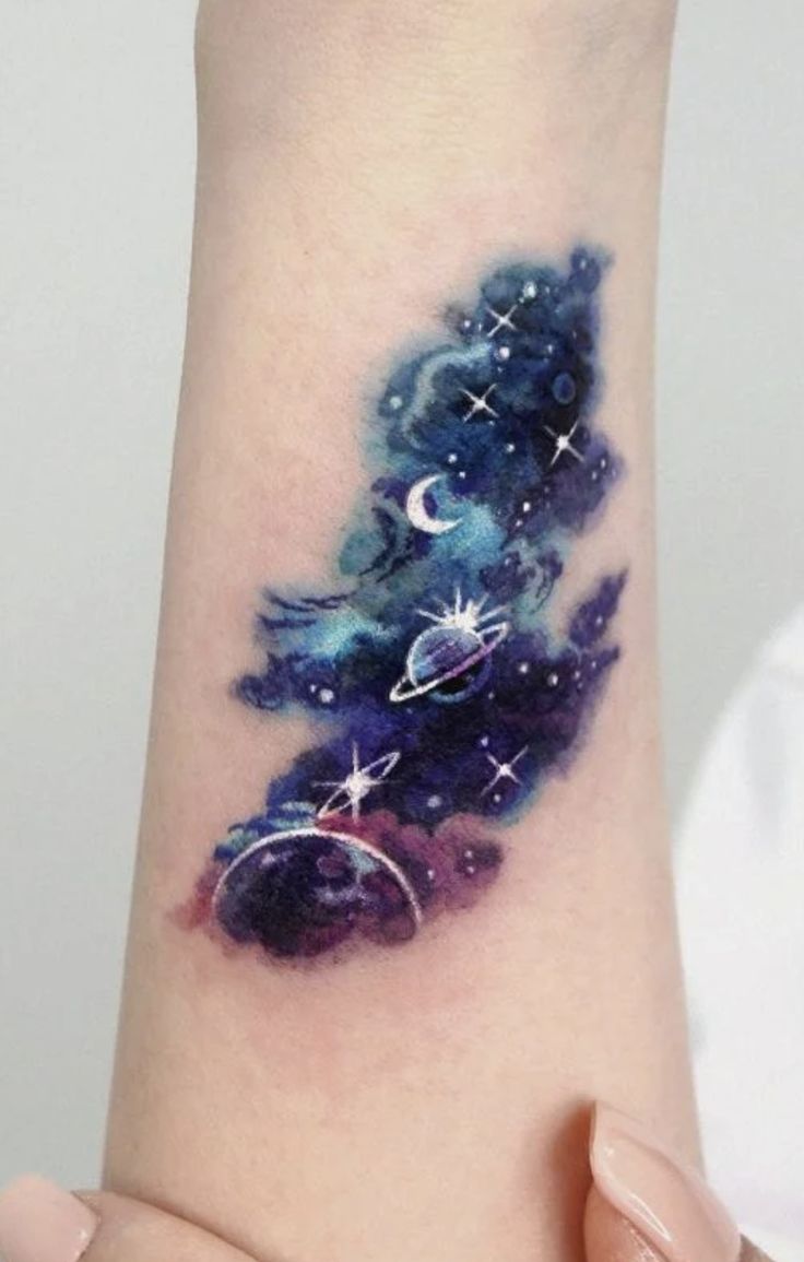 a woman's arm with a watercolor painting on it and stars in the sky