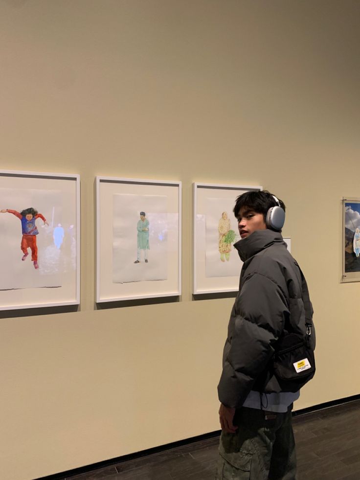 a man wearing headphones standing in front of pictures on the wall with his back to the camera