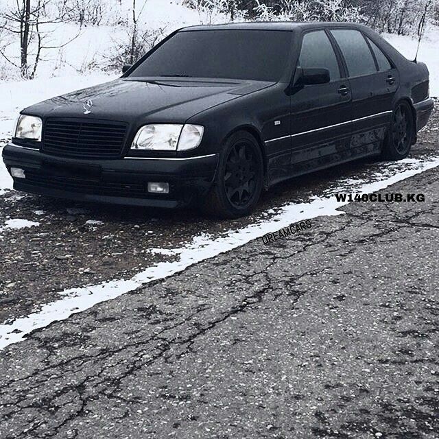 a black car parked on the side of a road next to snow covered grass and trees