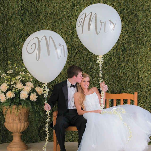 a bride and groom sitting on a bench with two balloons in the shape of mr and mrs