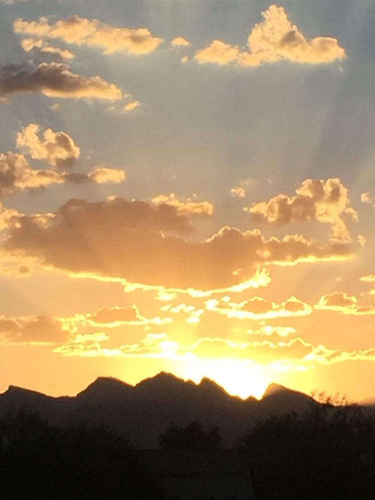 the sun is setting behind some mountains and clouds in the sky, with an airplane flying low to the ground