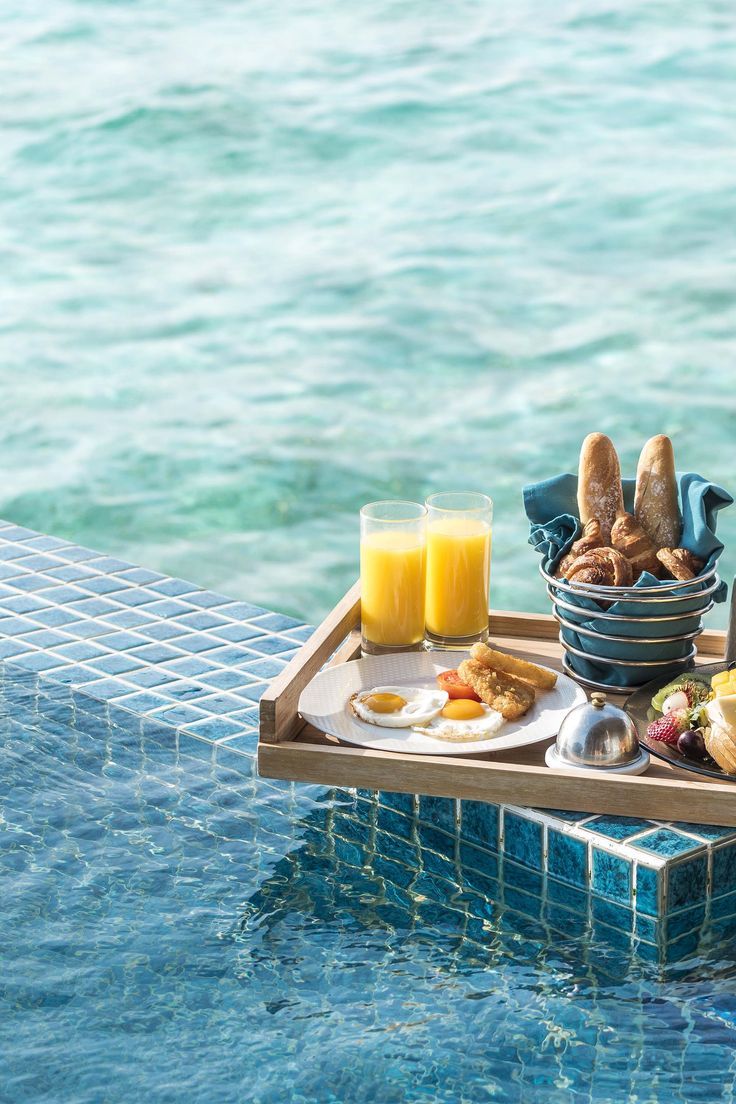 an assortment of food on a tray next to a swimming pool with blue tiles and water