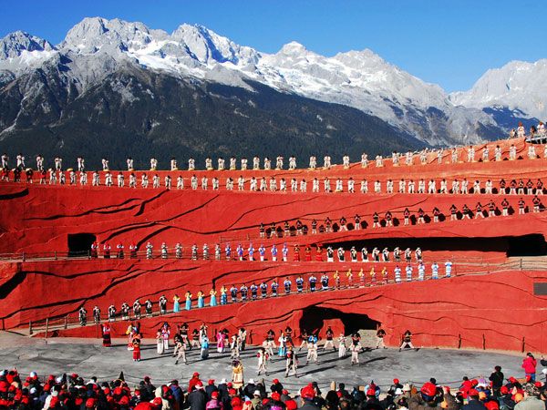 a large group of people standing on top of a red wall with mountains in the background