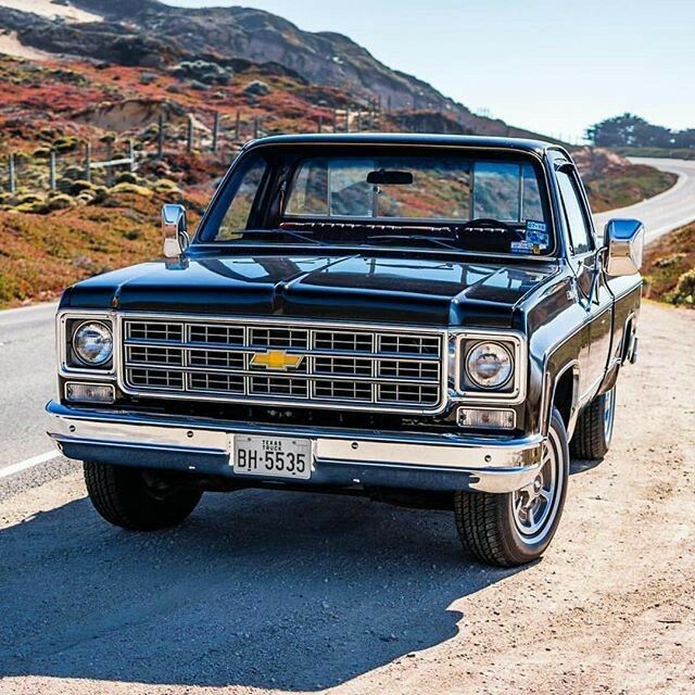 an old pickup truck is parked on the side of the road in front of some hills