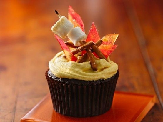 a cupcake with white frosting and fall leaves on top sitting on a plate