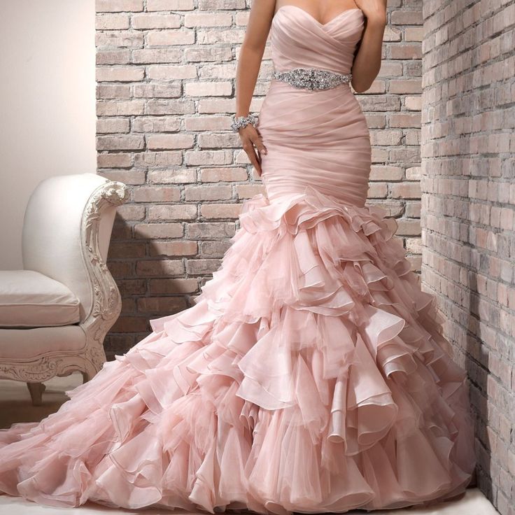 a woman in a pink dress is standing near a brick wall and posing for the camera