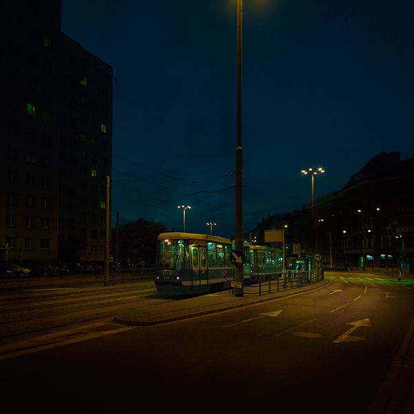 a bus driving down the street at night time with its lights on and buildings in the background