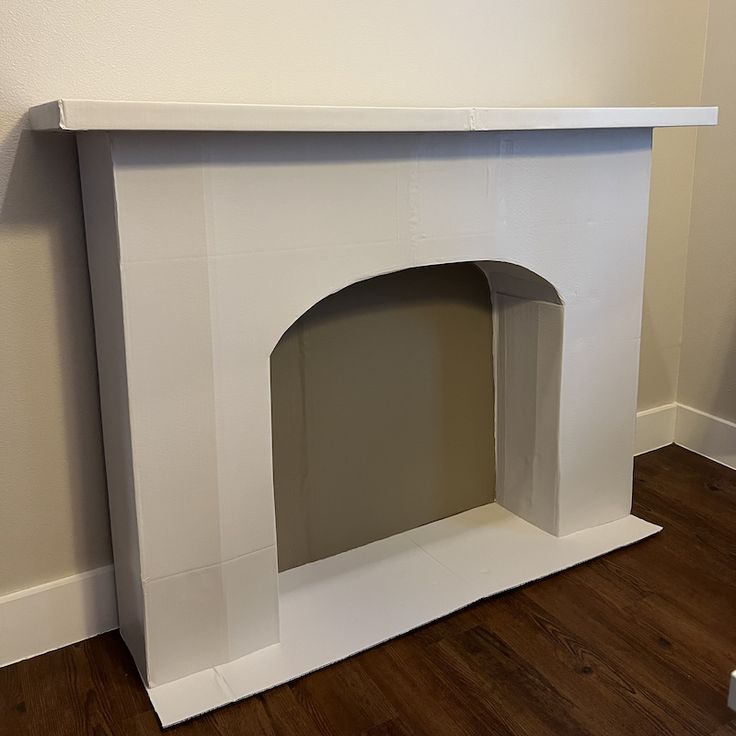 an empty white fireplace in a room with hard wood flooring