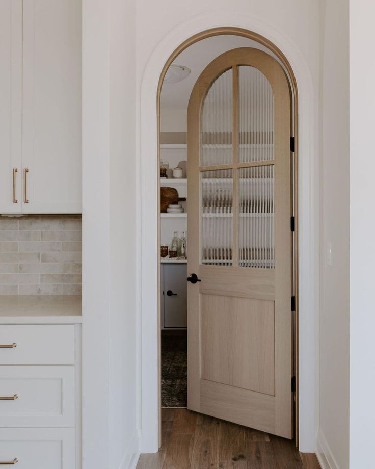 an arched wooden door in a white kitchen