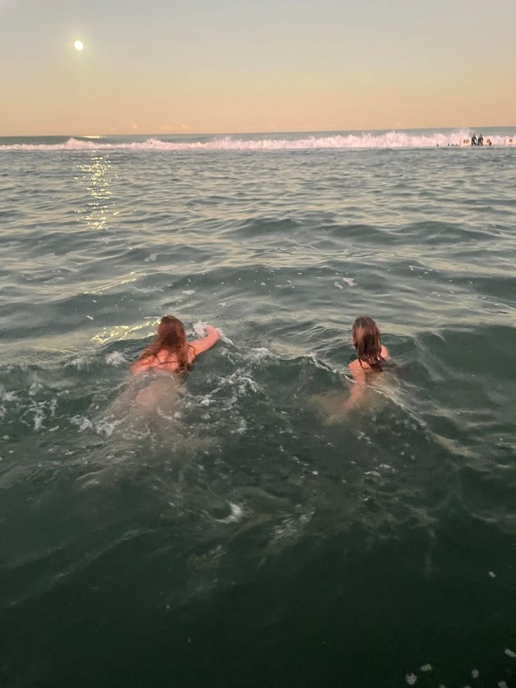 two people swimming in the ocean at sunset