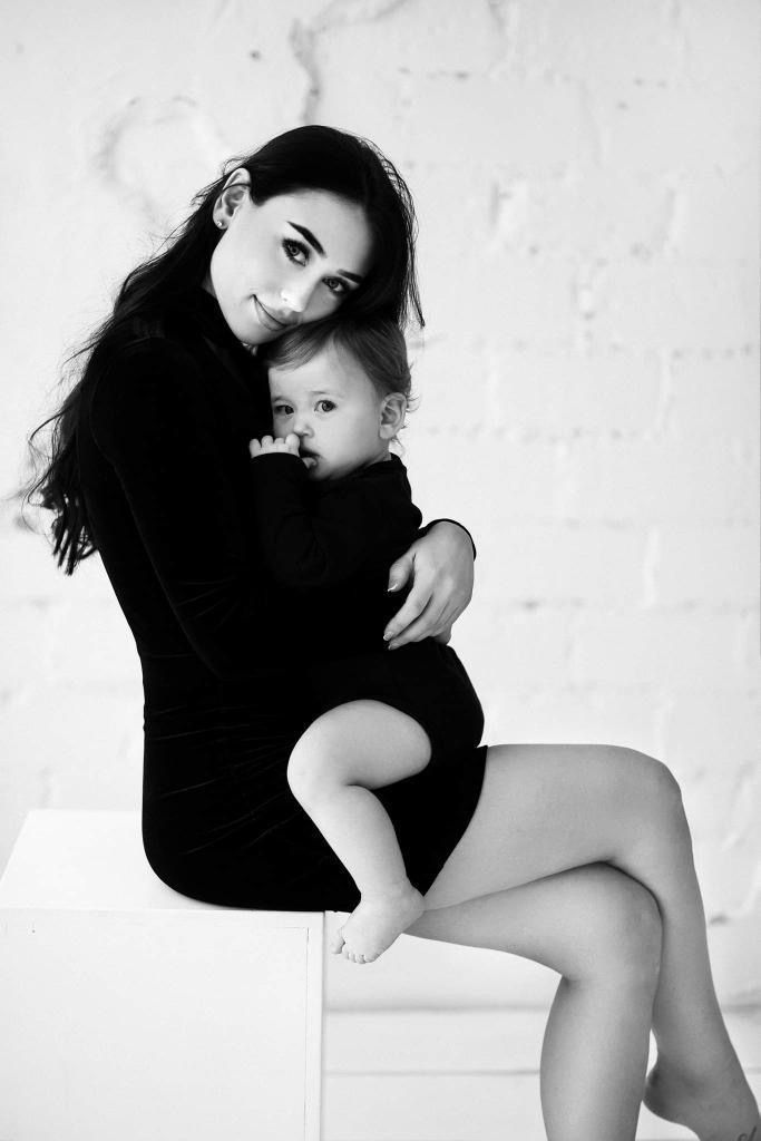 a woman holding a baby while sitting on top of a white table next to a brick wall