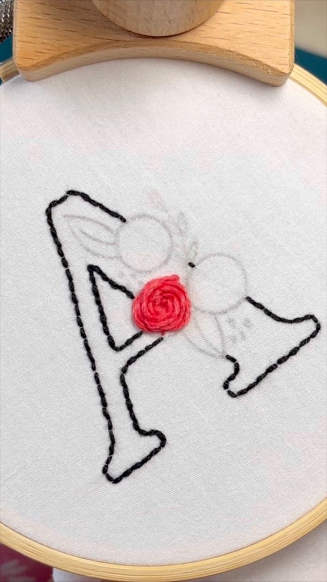 a close up of a embroidery on a wooden hoop with a red rose in it