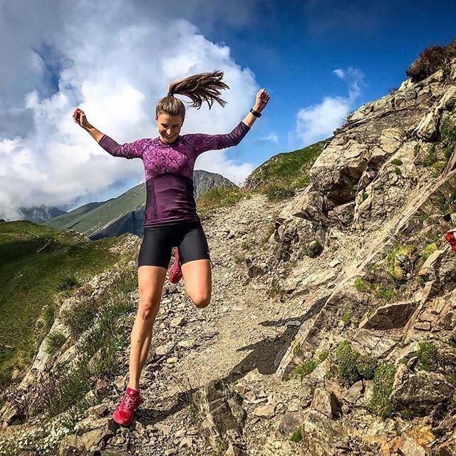 a woman running down a rocky trail on top of a mountain with her hair blowing in the wind