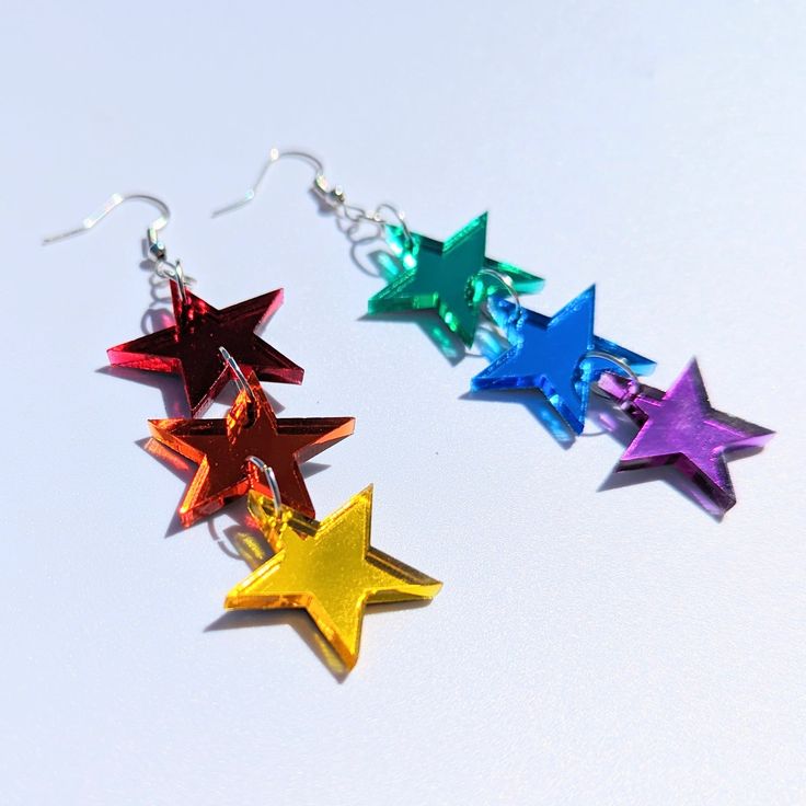 three different colored stars are hanging from silver earwires