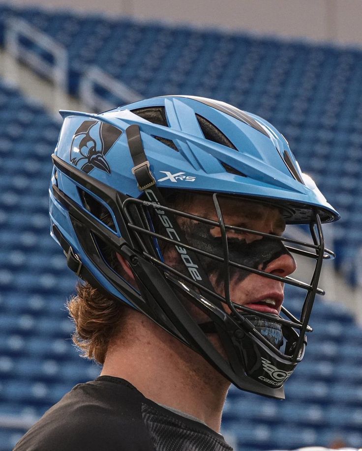 a close up of a person wearing a catchers helmet on a baseball field with bleachers in the background