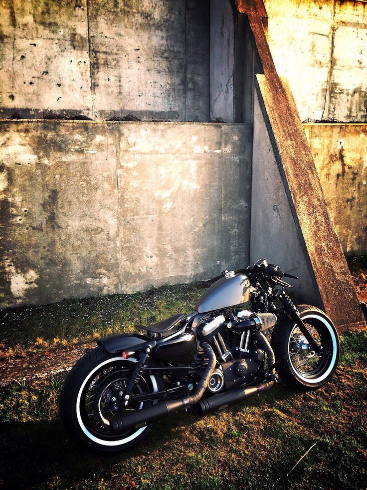 a black motorcycle parked in front of a concrete wall next to a wooden pole and grass