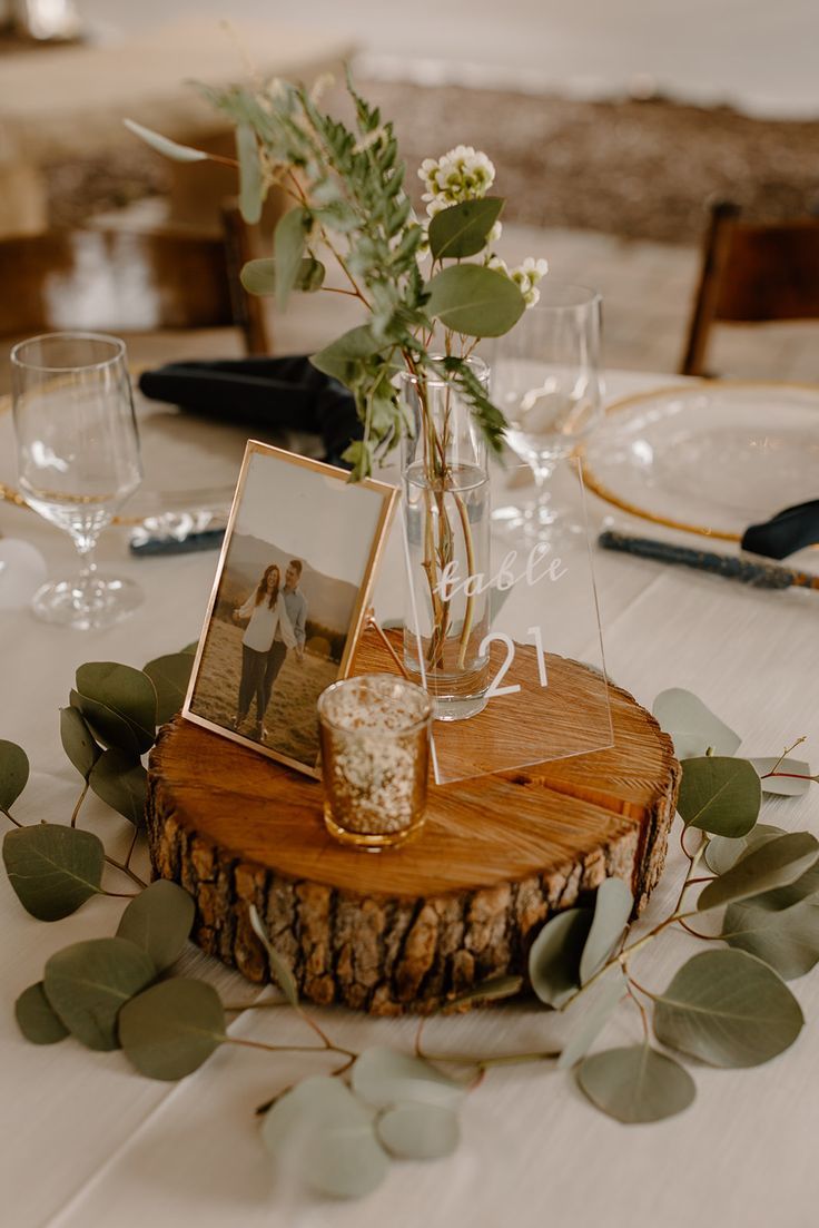 a wooden table topped with a vase filled with flowers and greenery next to pictures