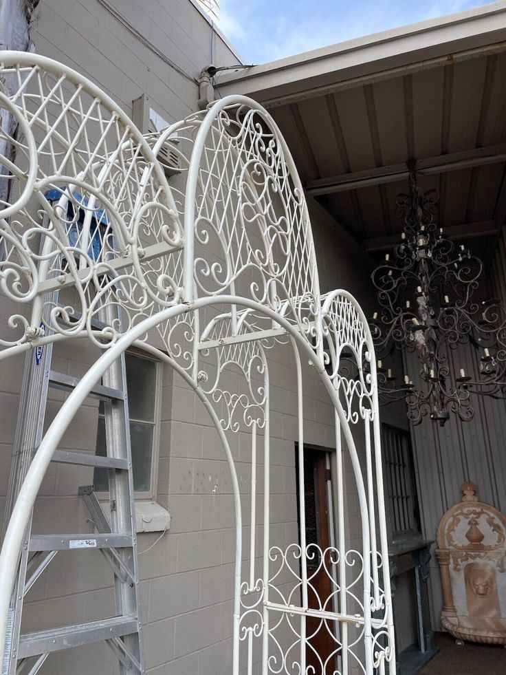 a white metal arch with chandelier hanging from it's side and another light fixture in the background