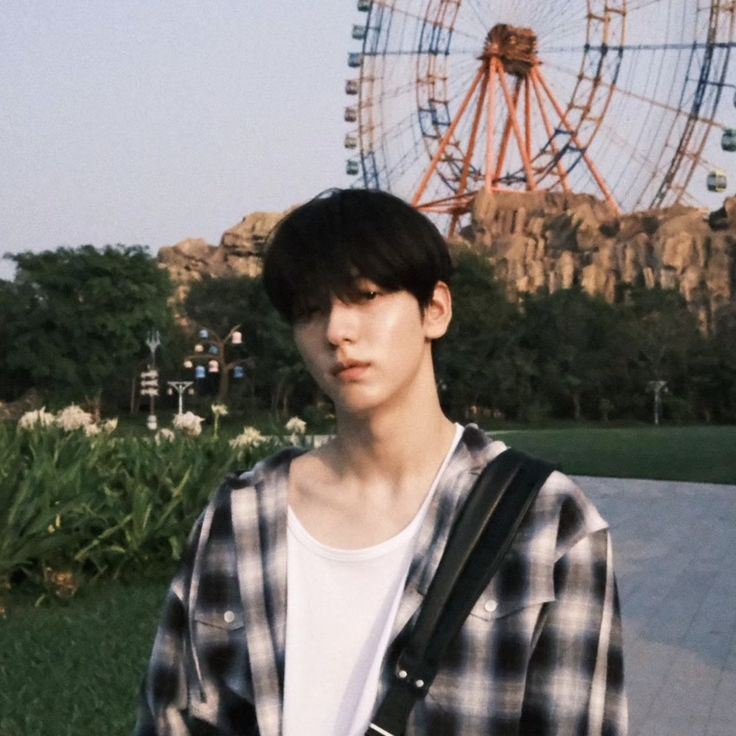 a young man standing in front of a ferris wheel with his hand on his hip