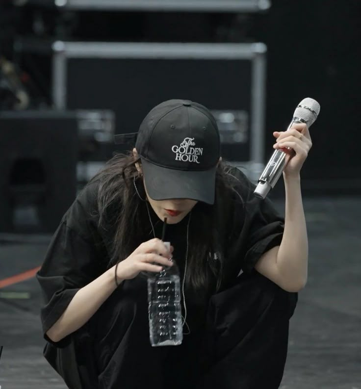 a woman kneeling down with a microphone in her hand while holding a water bottle up to her face