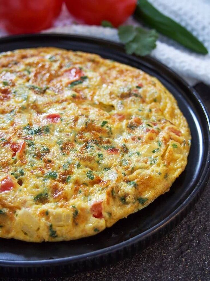 an omelet on a black plate with tomatoes in the background