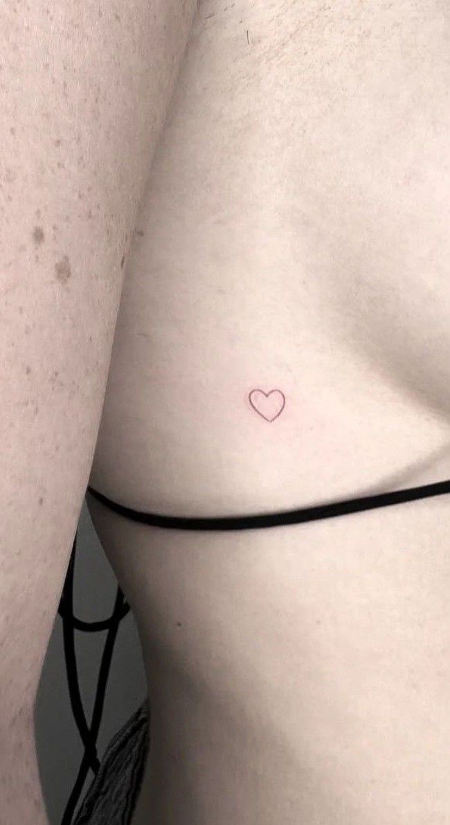 a small heart tattoo on the side of a woman's stomach