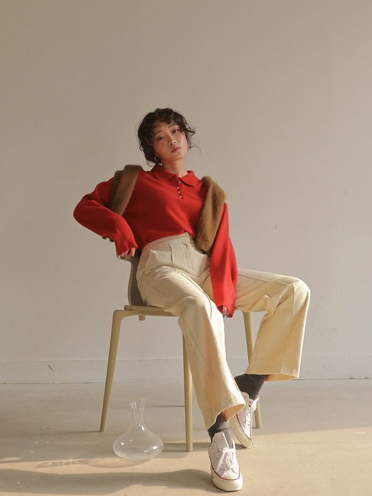 a woman is sitting on a chair with her legs crossed and she wears a red sweater