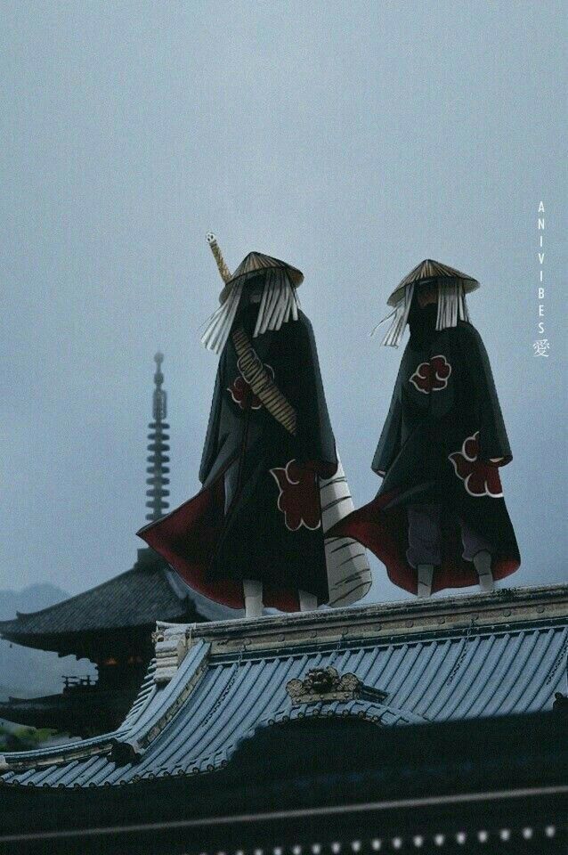 two people dressed in black and red standing on top of a roof with umbrellas