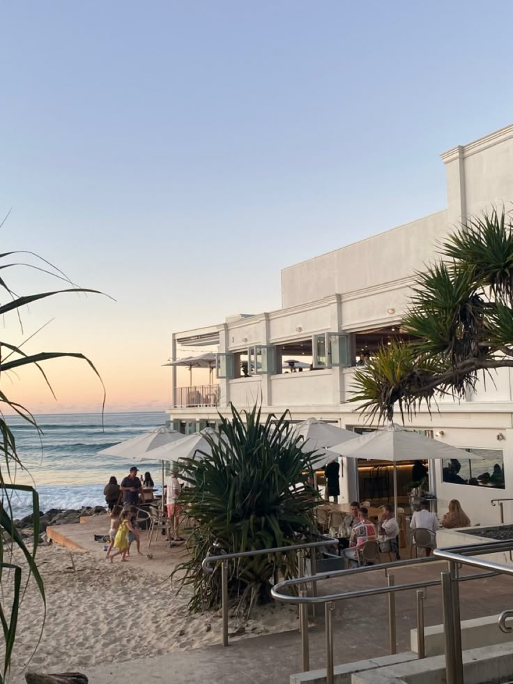 people are sitting on the beach at sunset