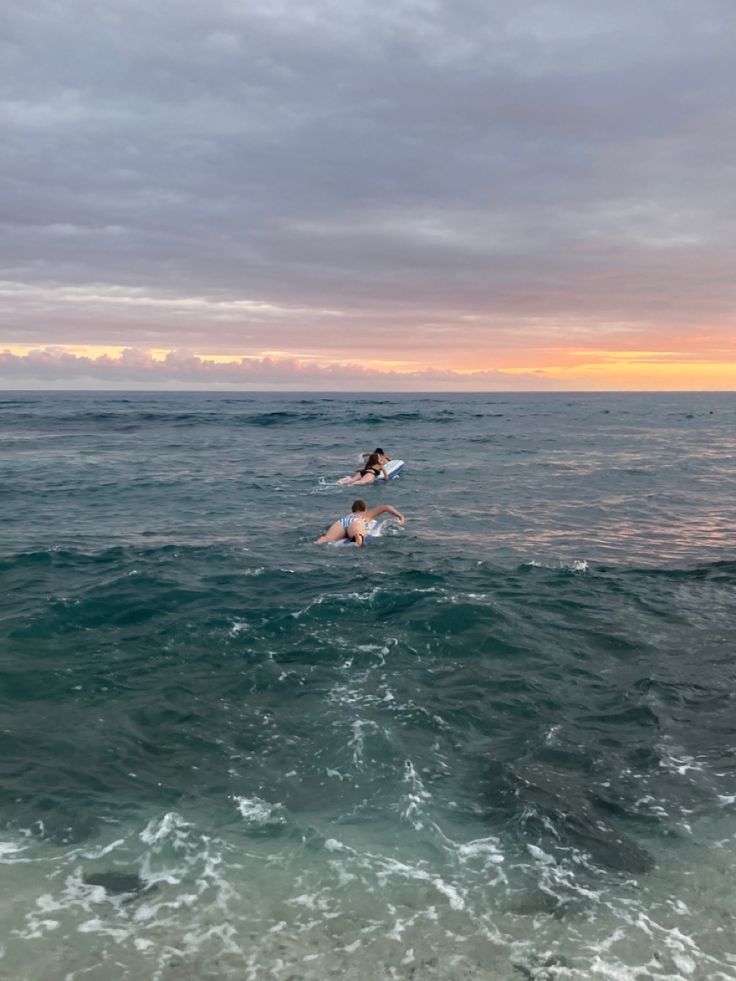 two surfers in the ocean at sunset with one jumping off his surfboard into the water