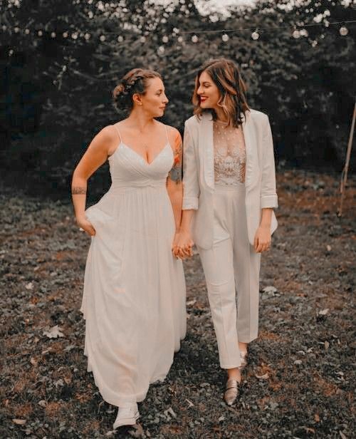 two women standing next to each other in the woods holding hands and looking at each other