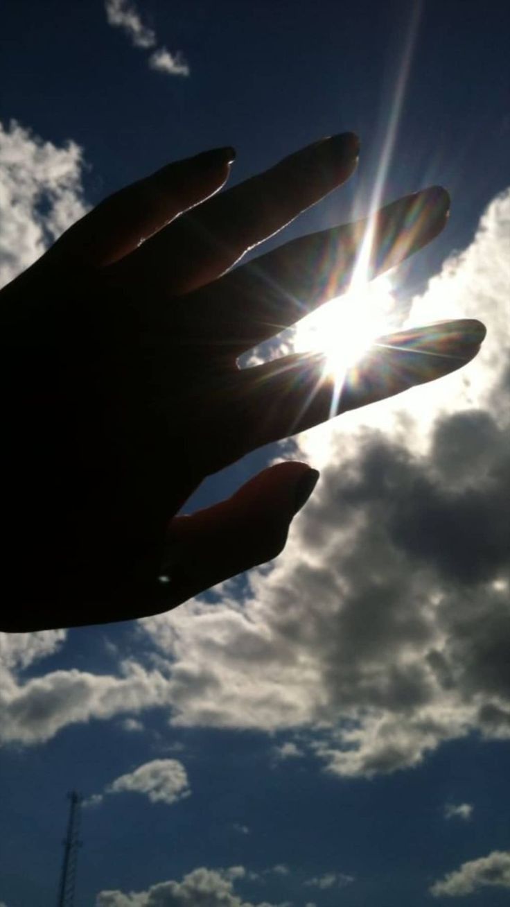 a person's hand reaching up into the sky with clouds in the back ground