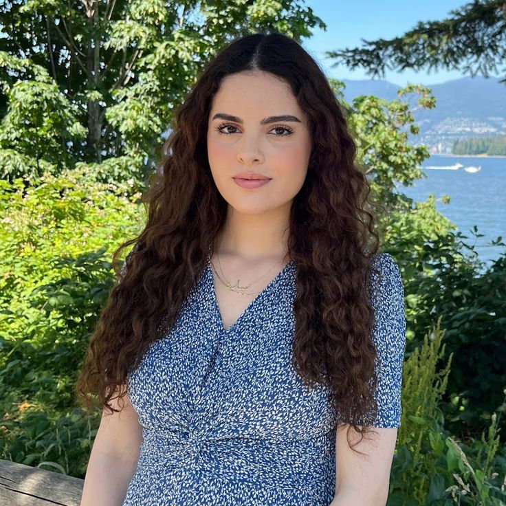 a woman standing in front of some trees with her hands on her hips and looking at the camera