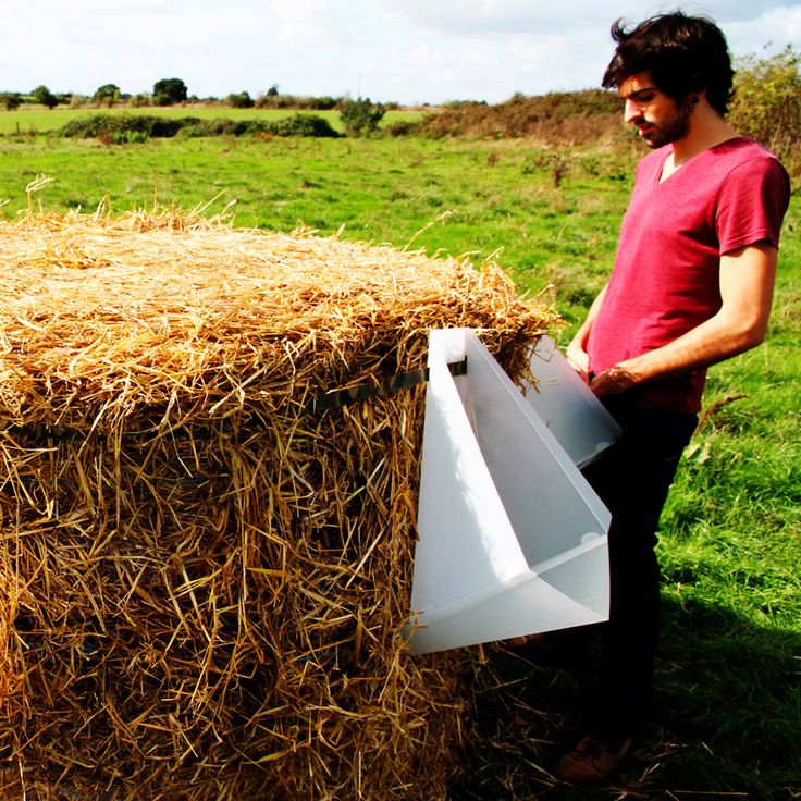 a man standing next to a bale of hay holding an item in his hand