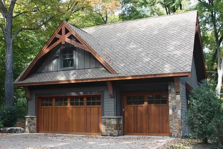 a two car garage with stone and wood trimmings on the roof, surrounded by trees