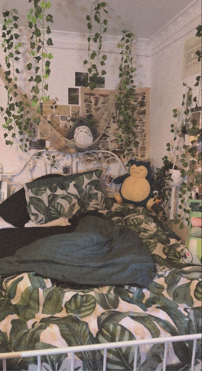 an unmade bed with plants hanging from the ceiling and a teddy bear on top