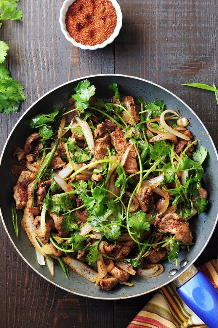 a pan filled with meat and vegetables on top of a wooden table next to utensils