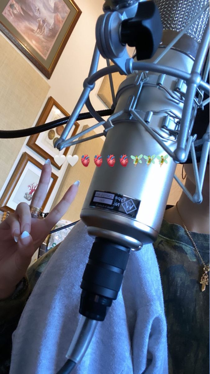 a woman is sitting in front of a microphone with her hand up to the camera