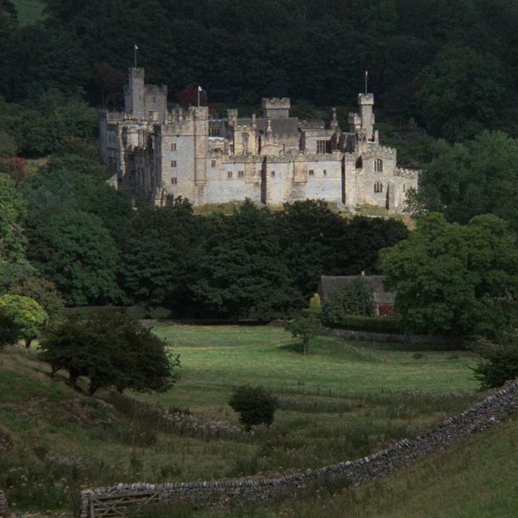 an old castle sits on top of a hill surrounded by trees and grass in the foreground