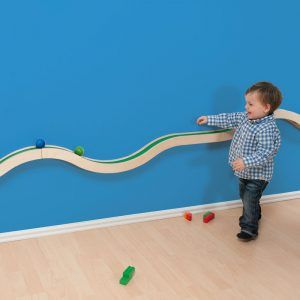 a young boy playing with a wooden train set on the floor in front of a blue wall