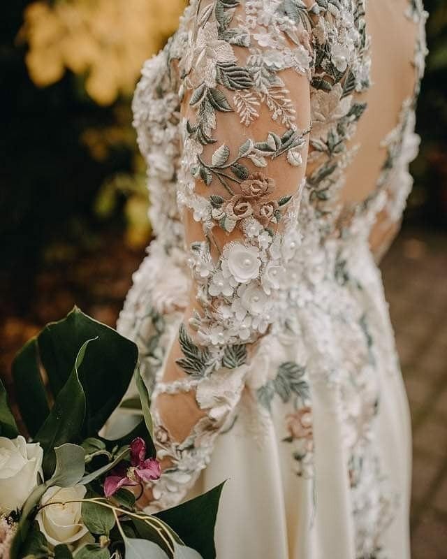 the back of a woman's dress with flowers and leaves on her shoulders, holding a bouquet