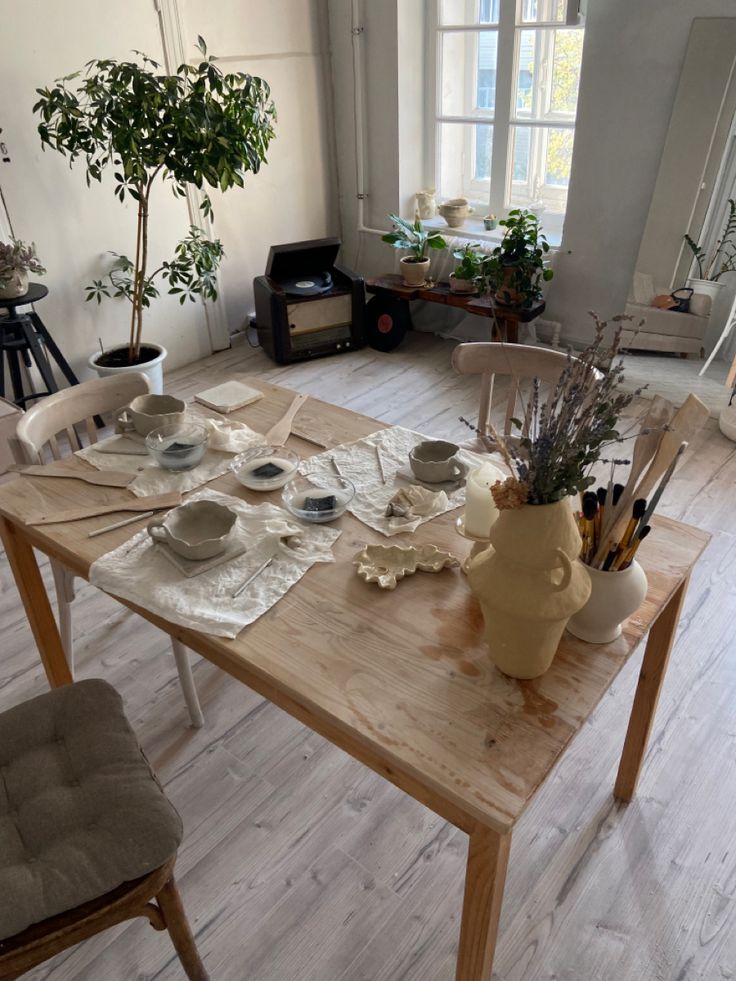 a wooden table topped with plates and bowls next to a potted plant on top of a hard wood floor