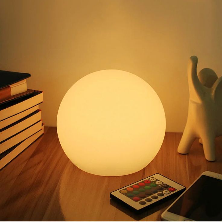 a white lamp sitting on top of a wooden table next to a cell phone and books