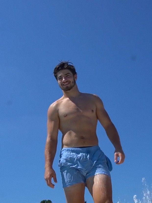 a shirtless man riding a surfboard on the beach