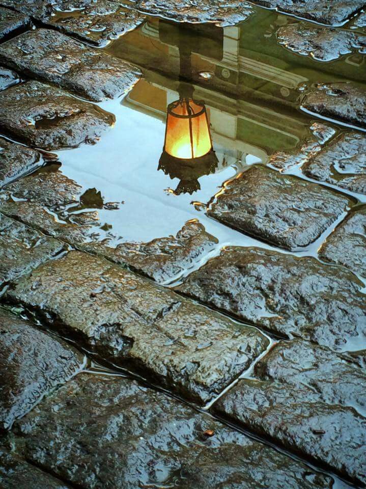 a street light reflected in puddles of water on cobblestone pavement at night