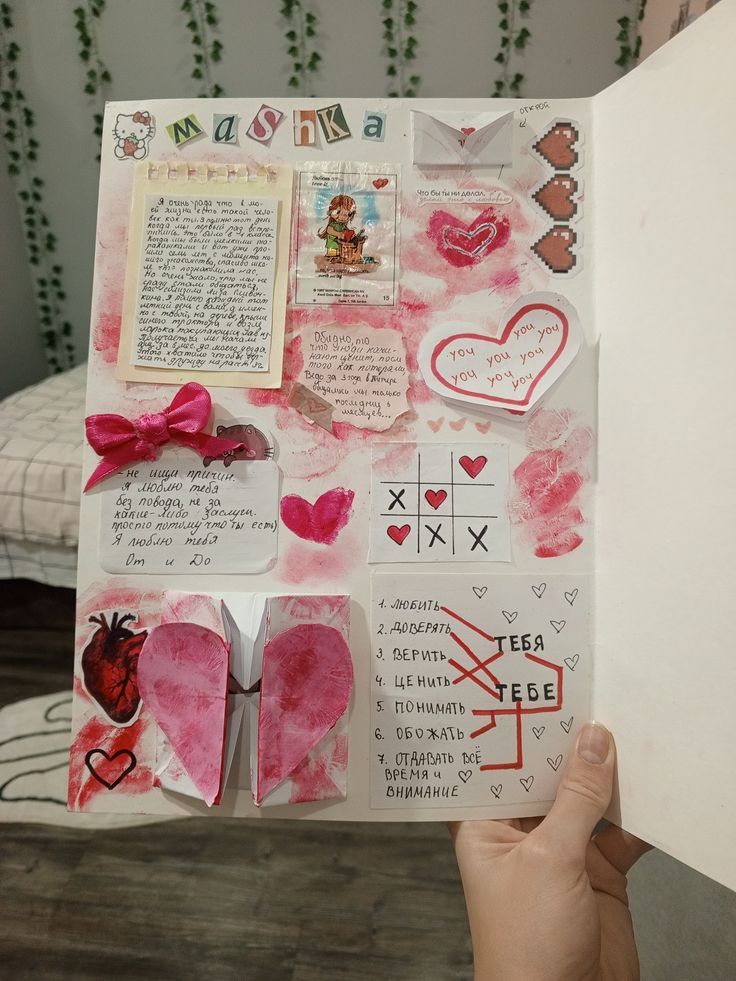 someone is holding up a scrapbook with hearts and other things on it in front of a bed