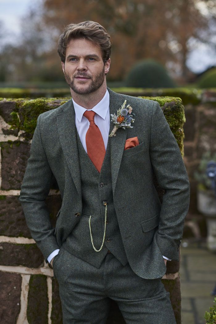 a man in a suit and tie standing next to a brick wall with moss growing on it