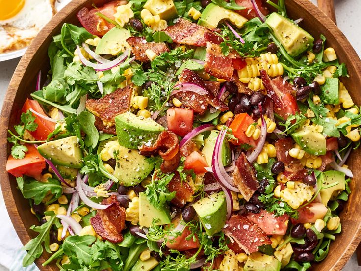 a wooden bowl filled with salad and dressing on top of a white tablecloth next to bread