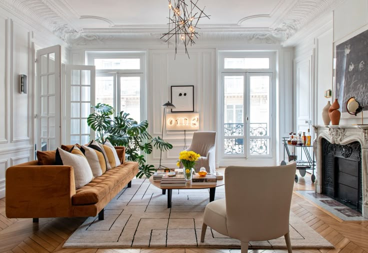 a living room filled with furniture and a fire place under a chandelier on top of a hard wood floor